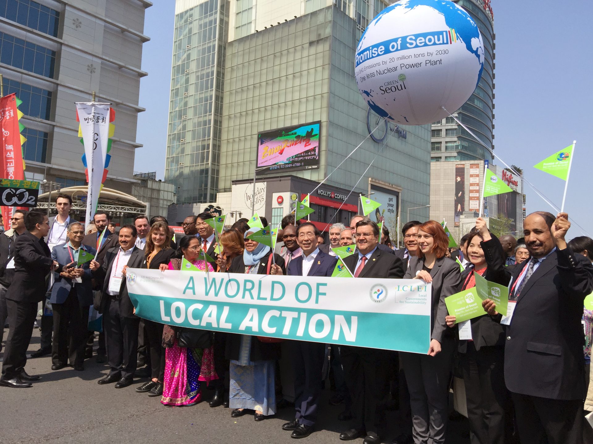 ICLEI World Congress banner reading A World of Local Action, with a huge group of people parading behind it on the street of Seoul, with a large balloon floating above reading Promise of Seoul.