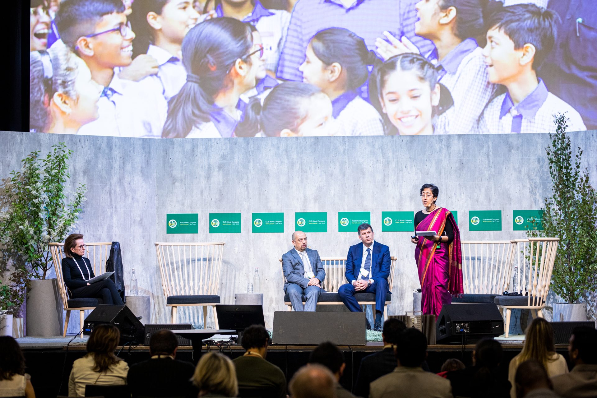 A group on panelists on stage at the ICLEI World Congress with a woman speaking to the audience.